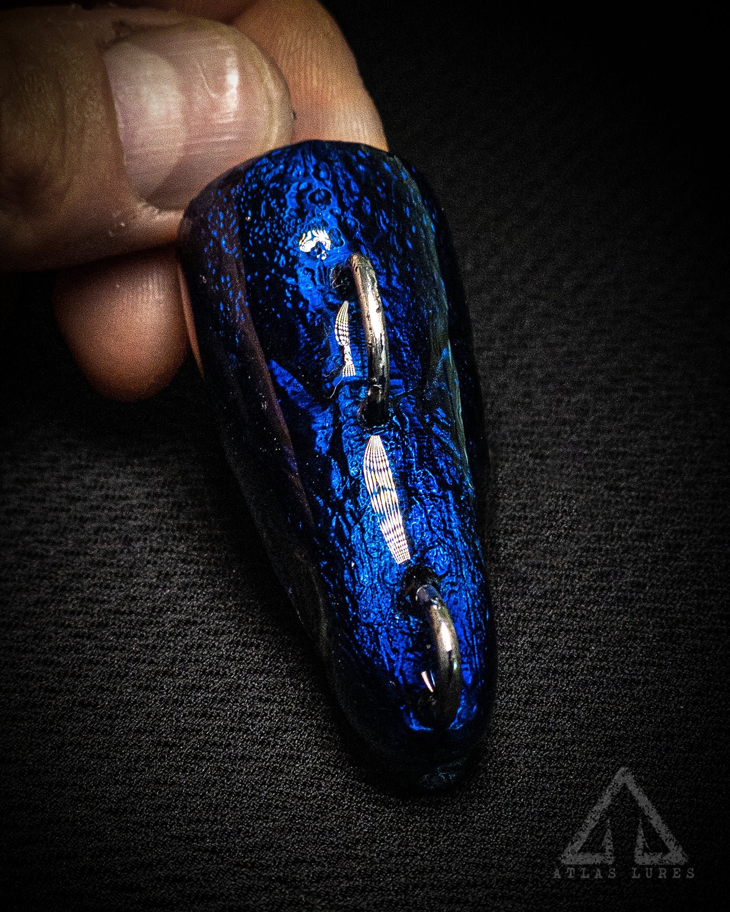 Blue and black textured object held in a hand against a dark background
