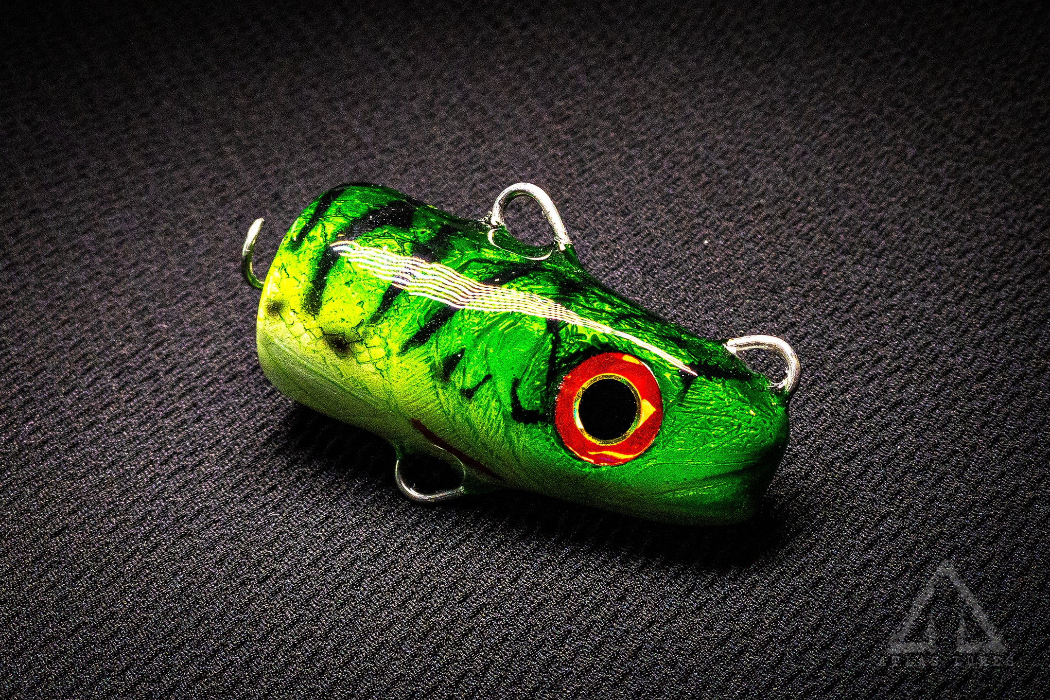 Green fishing lure with red eye on a black textured background