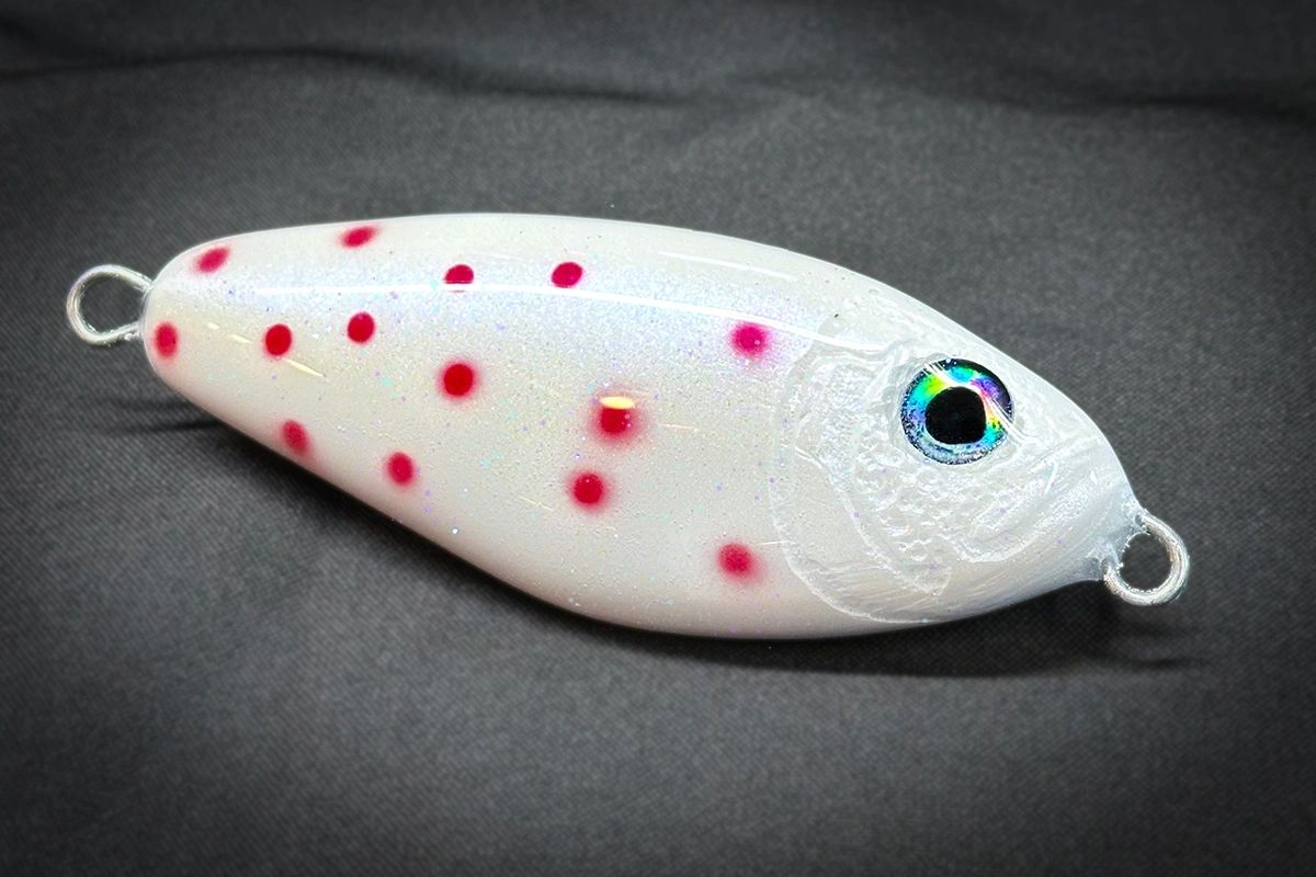 White fishing lure with red spots and a colorful eye on a gray background