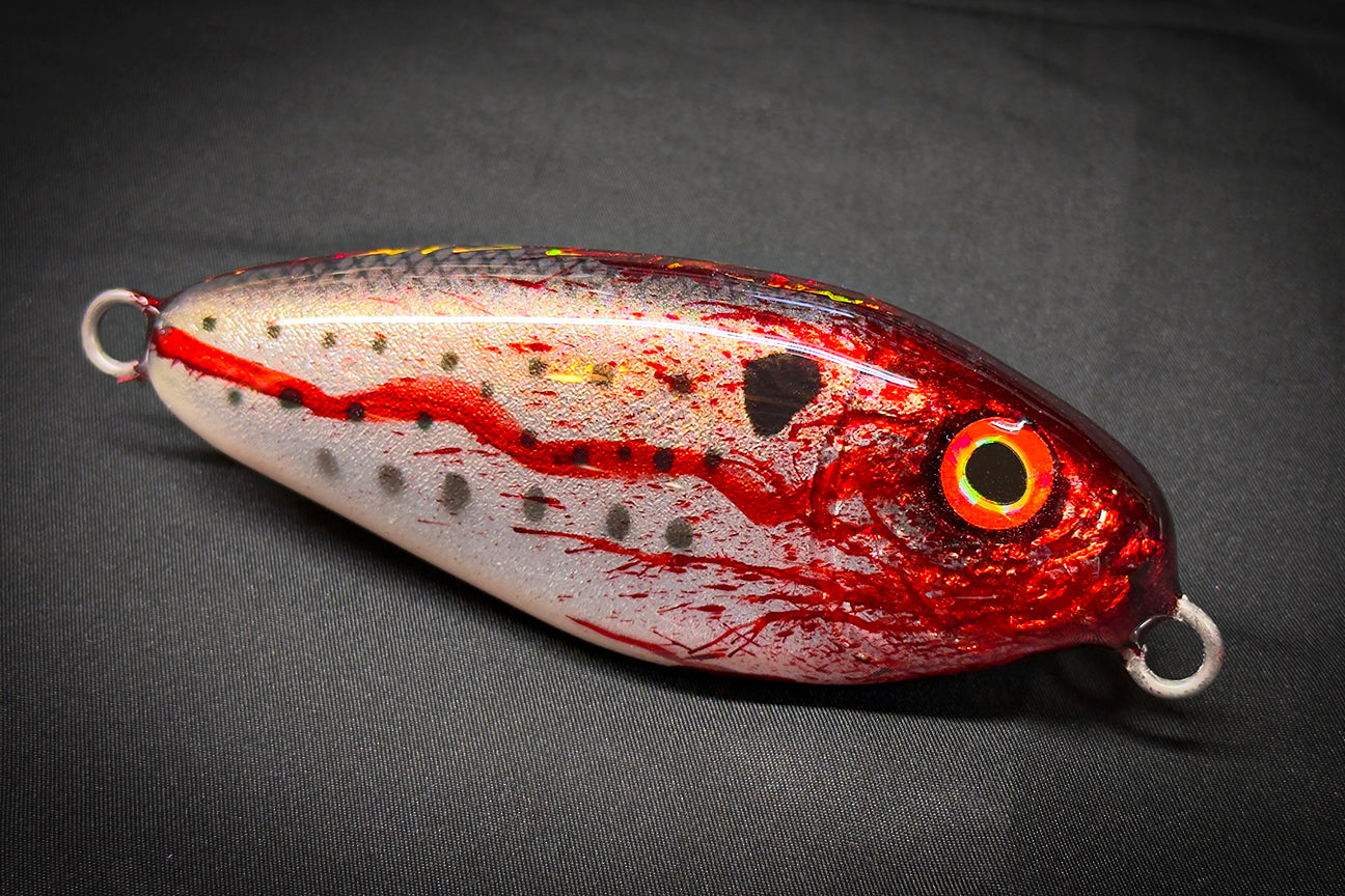 Fishing lure with red and silver design on a dark background