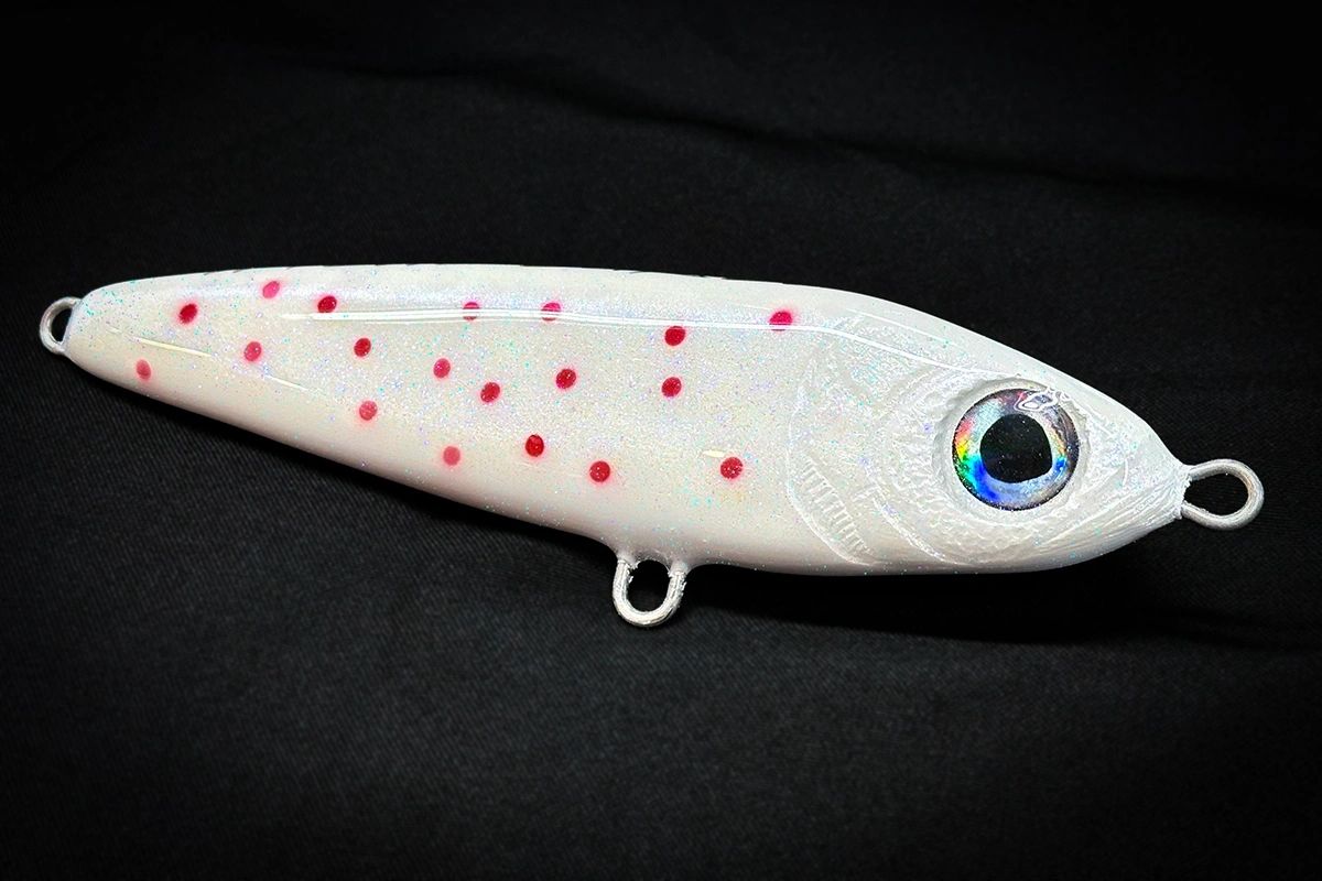 White fishing lure with red spots on a black background