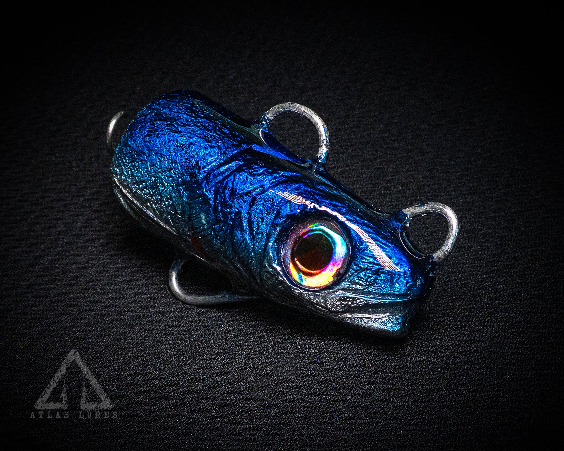 Blue metallic fishing lure with a rainbow eye on a black background