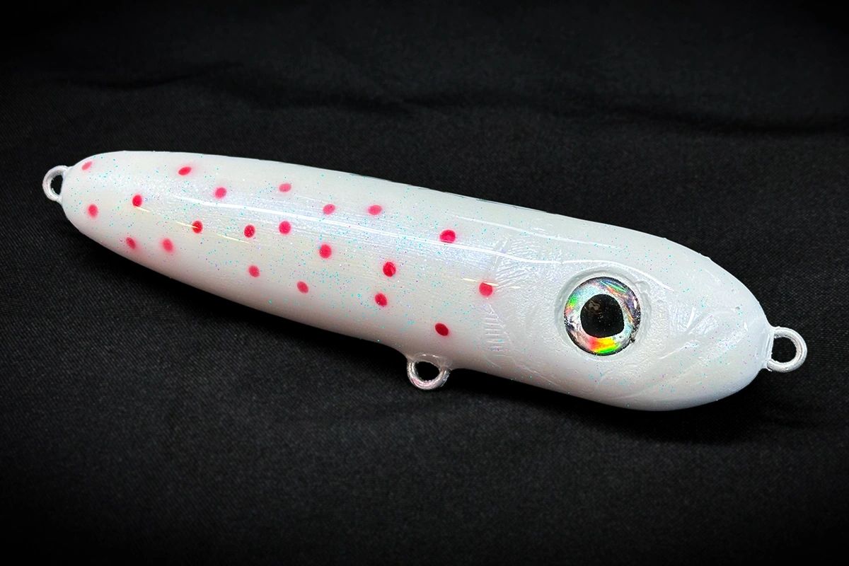 White fishing lure with red spots on a black background
