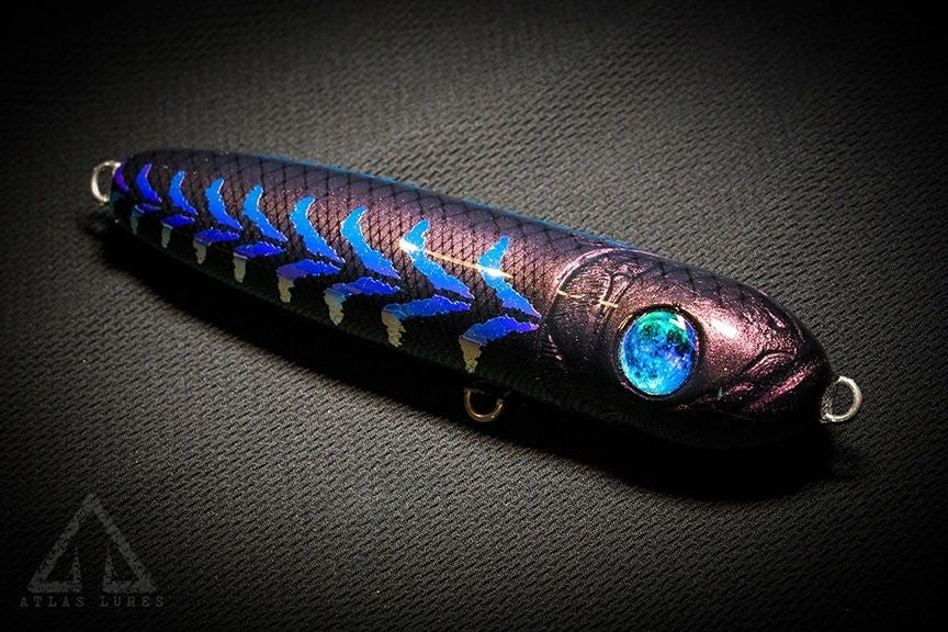 Fishing lure with metallic purple body and blue accents on a dark background