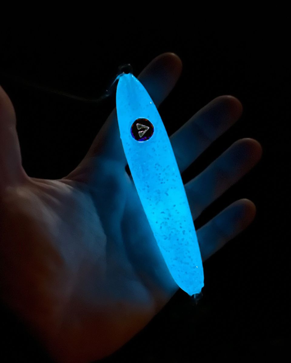 Blue glowing fishing lure held in a hand against a dark background